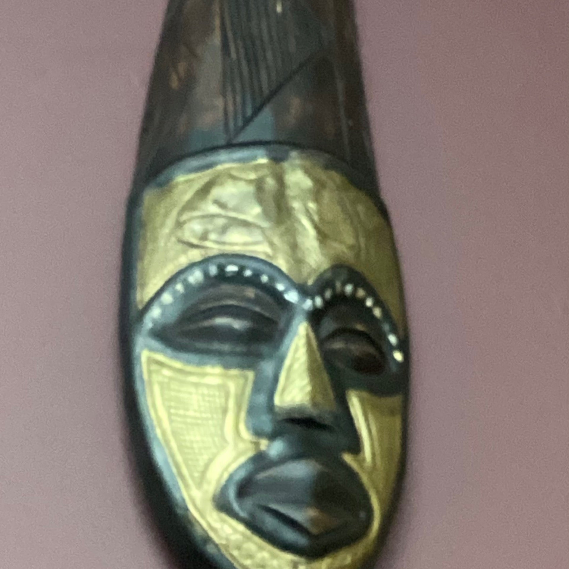 Hand carved African mask with golden face and tall headpiece (back wall)